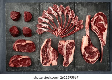 Assorted high-quality cuts of raw beef steaks, including ribeye, filet mignon, and tomahawk, arranged on a slate surface.