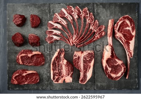 Assorted high-quality cuts of raw beef steaks, including ribeye, filet mignon, and tomahawk, arranged on a slate surface.