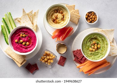 assorted hummus dips in bowls, served with fresh vegetables and crackers. Traditional hummus, beetroot hummus and avocado hummus. Healthy summer vegan snack. top view. - Powered by Shutterstock