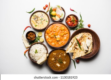 Assorted indian food for lunch or dinner, rice, lentils, paneer butter masala, palak panir, dal makhani, naan, green salad, spices over moody background. selective focus
