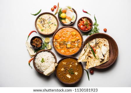 Assorted indian food for lunch or dinner, rice, lentils, paneer butter masala, palak panir, dal makhani, naan, green salad, spices over moody background. selective focus
