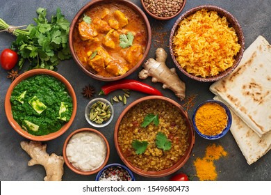 Assorted Indian food on a dark rustic background. Traditional Indian dish Chicken tikka masala, palak paneer, saffron rice, lentil soup, pita bread and spices. Top view, flat lay