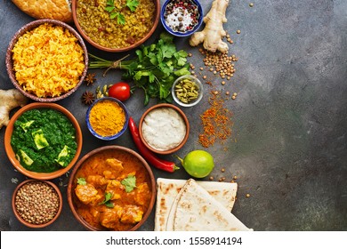 Assorted Indian food on a dark rustic background. Set traditional Indian dishes - Chicken tikka masala, palak paneer, saffron rice, lentil soup, pita bread and spices. View from above,copy space