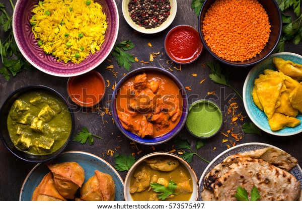 Assorted indian food on dark wooden background.\
Dishes and appetizers of indian cuisine. Curry, butter chicken,\
rice, lentils, paneer, samosa, naan, chutney, spices. Bowls and\
plates with indian\
food