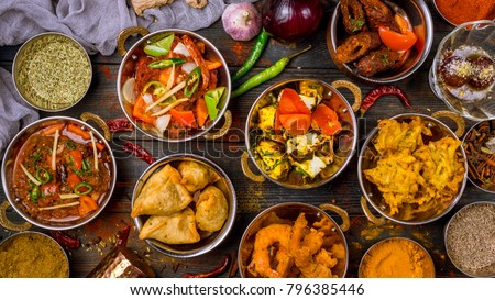 Assorted indian food set on wooden background. Dishes and appetisers of indeed cuisine, rice, lentils, paneer, samosa, spices, masala. Bowls and plates with indian food top view