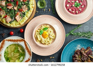 Assorted Italian food on a dark background: carbonara pasta, salmon pizza, beetroot risotto, homemade chicken broth and salad. Top view flat lay food