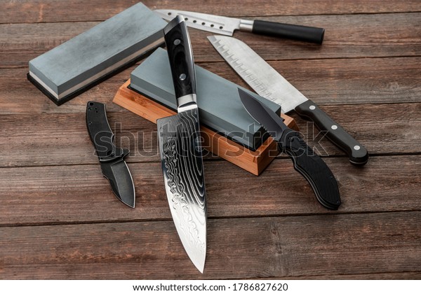 Assorted knives and sharpening stones on a rustic wooden table, top view. Jackknife, cheese knife, Santoku and chef's knife.
