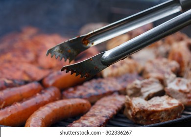 Assorted meat from chicken and pork and sausages on barbecue grill with barbecue tongs