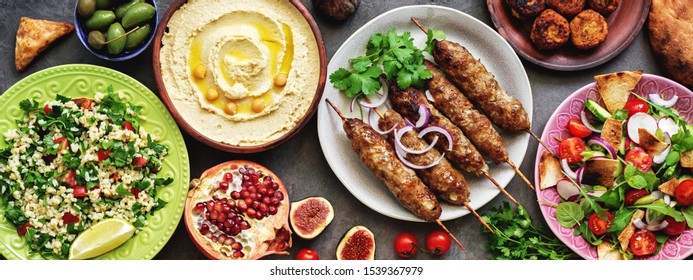 Assorted Middle Eastern and arabic dishes on a dark rustic background, border. Hummus,tabbouleh, salad Fattoush,pita,meat kebab,falafel,baklava,pomegranate. Halal food.Top view, flat lay, copy space.