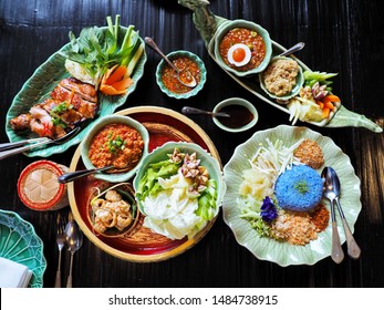 Assorted mix variety of colorful spicy sweet sour traditional popular authentic Thai food served on conservative style plates on wooden table e.g. street food as Pad Thai, Fried rice, and spicy salad