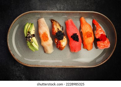 Assorted Nigiri sushi on a plate, on dark concrete. Top view