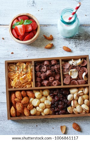 Assorted nuts, cereal and raisin in a rustic box, strawberry and milk on wooden table. Top view of healthy breakfast for children.
