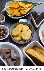 Assorted party snacks on table featuring chocolate cream sandwich biscuits, sugar coated heart cookies, wafer chocolates, chocolate coated caramel balls, salted crackers, and crispy potato chips.