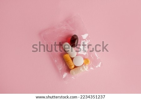Assorted pharmaceutical medicine pills, tablets and capsules in small sachet on pink background