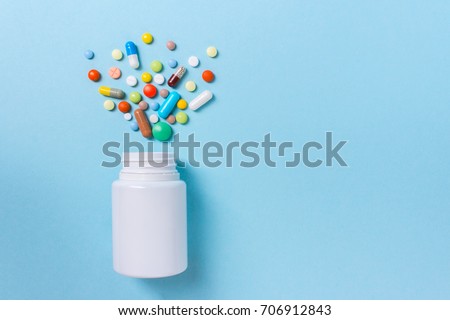 Assorted pharmaceutical medicine pills, tablets and capsules and bottle on blue background. Copy space for text