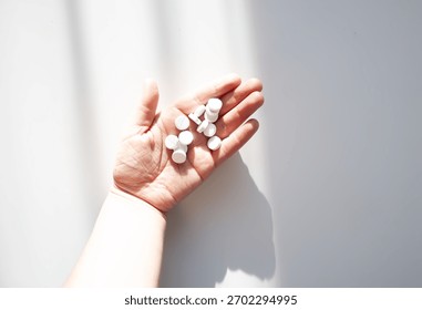 Assorted pills in a hand under diffused light. Aesthetic representation of healthcare and wellness.