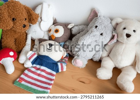 Assorted plush stuffed animals and dolls arranged on a wooden floor, including a brown teddy bear, gray elephant, white bear, and owl.