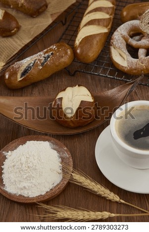 Assorted pretzels and lye bread with flour, wheat ears, and coffee arranged on a rustic wooden table.