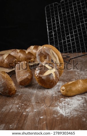Assorted pretzels and lye bread rolls on a floured wooden table with a cooling rack and dark rustic background.