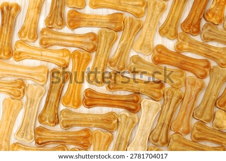 Assorted rawhide dog bones scattered across a light wooden surface as a pet treat background.
