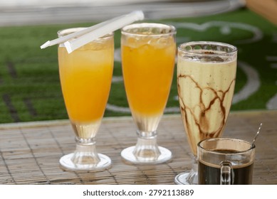  Assorted refreshing beverages including fresh orange juice glasses, avocado chocolate milkshake, and a hot cup of black coffee on a bamboo table.