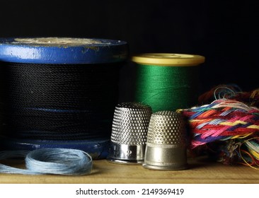 ASSORTED SEWING THREADS WITH AN OLD WOODEN VINTAGE SPOOL, THIMBLES AND A COLORFUL BRAID