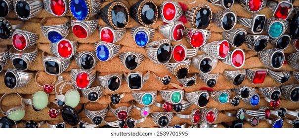 Assorted silver rings with red, blue, black, and green gemstones on display. - Powered by Shutterstock