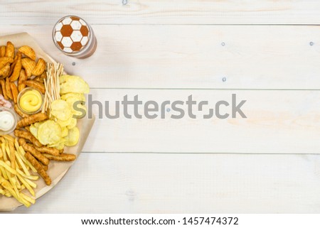 Assorted snacks and beer with a soccer ball on a beer foam on wooden background. Empty space for text. Top view.