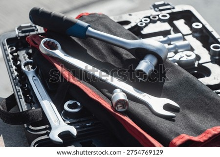 Assorted socket wrenches and ratchet wrench with rubber grip handle neatly arranged in a red fabric tool roll pouch on black plastic case. Mechanic tools, automotive repair kit and hardware organizer