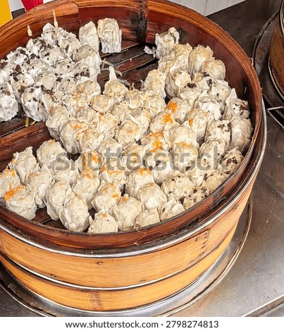 Assorted Steamed Dim Sum Dumplings in a Traditional Bamboo Steamer Basket.
A large, round bamboo steamer basket holds an assortment of fresh steamed Dim Sum, some topped with grated carrots and others with black fungus filling, ready to be eaten.