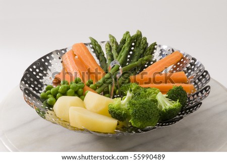 Assorted steamed vegetables in a steamer. White background.