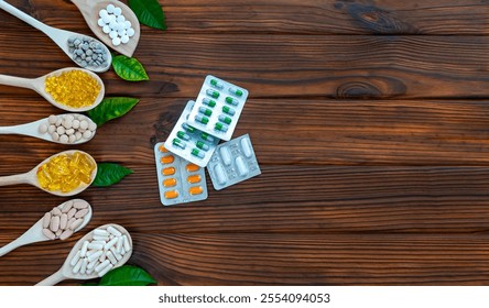 Assorted Supplements and Blister Packs on Wood. A variety of pills, capsules, and tablets on wooden spoons with blister packs and green leaves over a rustic wooden surface.