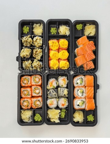 Assorted sushi rolls in black plastic takeout boxes, neatly arranged with ginger and wasabi on a white table, ideal for concepts of Japanese cuisine, delivery service, or modern healthy food lifestyle