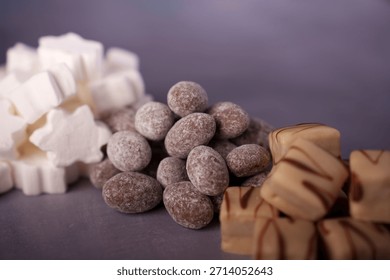 assorted sweets composition featuring white marshmallow stars, chocolate-coated almonds, and caramel cubes on a soft purple surface, selectivefocus, styled, appetizing, pattern, shapes, focus, scene