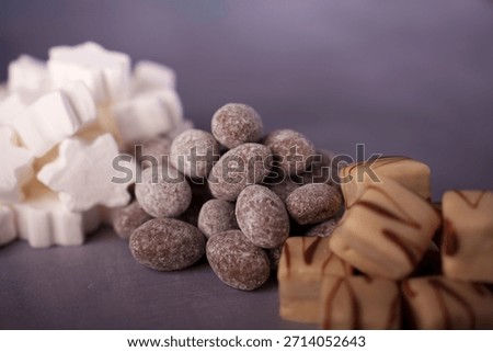 assorted sweets composition featuring white marshmallow stars, chocolate-coated almonds, and caramel cubes on a soft purple surface, selectivefocus, styled, appetizing, pattern, shapes, focus, scene