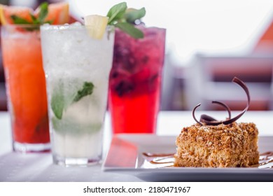 Assorted Three Types Of Lemonade, Classic Lemonade, Grapefruit Lemonade And Blackcurrant Lemonade. Drinks In Tall Glass Glasses With Ice, Lime Slices And Mint Leaves. The Dishes Are On A White Tablecl