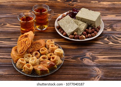 Assorted traditional eastern desserts with tea on wooden background. Arabian sweets on wooden table. Baklava, halva, rahat lokum, sherbet, nuts, dates, kadayif on plates. Space for text.