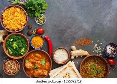 Assorted traditional Indian food on a dark background. Corner frame Indian dish Chicken tikka masala, palak paneer, saffron rice, lentil soup, pita bread and spices. 