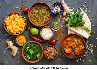 Assorted various Indian food on a dark rustic background. Traditional Indian dishes - Chicken tikka masala, palak paneer, saffron rice, lentil soup, pita bread and spices. Top view, flat lay