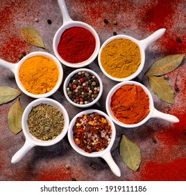 Assorted various spices on spoons on a dark background with laurel leaves.
