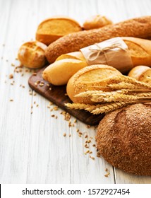 assortment of baked bread on white wooden background - Shutterstock ID 1572927454