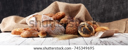 Assortment of baked bread and bread rolls on wooden table background.