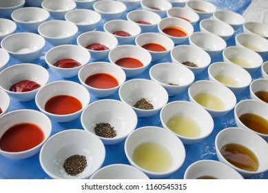 Assortment of basic food flavoring and seasoning ingredients ready for cooking. Sugar, Salt, Ketchup, Red Chili Sauce, Ground Black Pepper, Lime Juice, Fish Sauce in separate bowls on blue table.