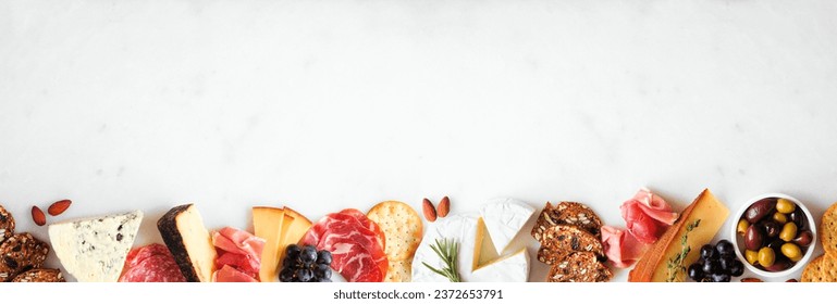 Assortment of charcuterie cheeses, meats and appetizers. Top view bottom border on a white marble background with copy space. - Powered by Shutterstock