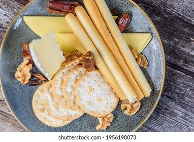 An Assortment Of Cheese And Crackers On A Round Blue Plate, With A Fancy Knife And Fork.