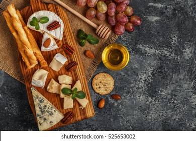 Assortment of cheese with honey, nuts and grape on a cutting board, top view. - Powered by Shutterstock