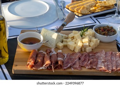 Assortment of cheese and processed meats on a wooden plate in a restaurant setting outdoors illuminated with natural light, realistic composition in a real setting, real food concept 
 - Powered by Shutterstock
