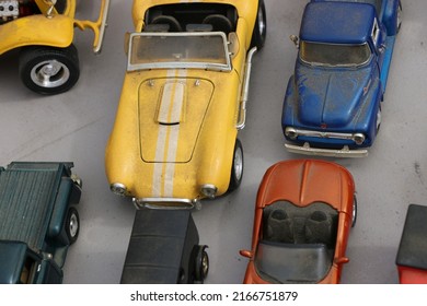 Assortment Of Collectible, Vintage Metal Toy Cars Arranged On A Table At A Garage Sale. A Yellow Convertible With A Racing Stripe Is In The Center.