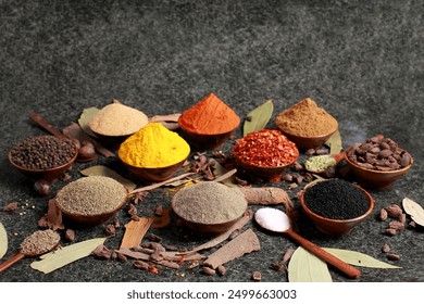 An assortment of colourful spices displayed in small bowls on a dark stone surface. The selection includes turmeric, red pepper flakes, black peppercorns, black cardamom, and various ground spices. - Powered by Shutterstock