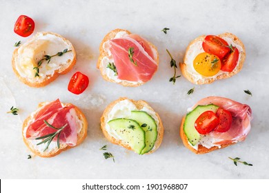 Assortment Of Cream Cheese Crostini Hors D'oeuvres With A Variety Of Toppings. Above View On A White Marble Background. Party Food Concept.